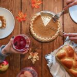 Cozy autumn table setting with pumpkin pie, bread, and drinks. Perfect for Thanksgiving vibes.
