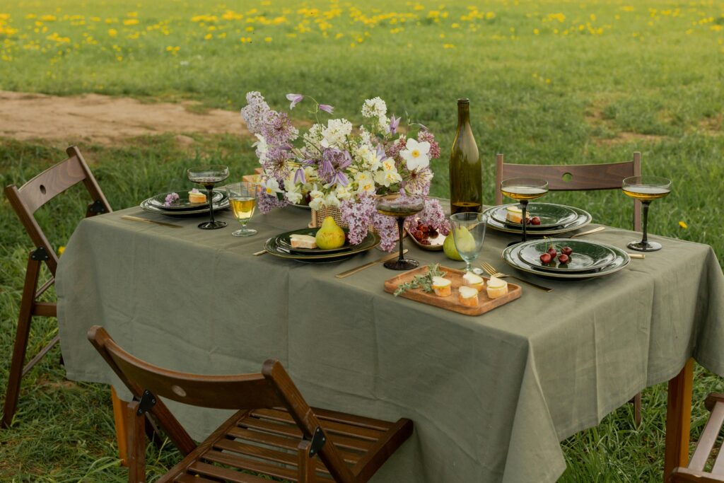 Elegant picnic table set with flowers and glassware in a lush field. Ideal for spring dining concepts.