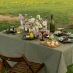 Elegant picnic table set with flowers and glassware in a lush field. Ideal for spring dining concepts.